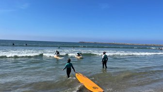 Surfer in einem Neoprenanzug geht ins Wasser, während andere auf ihren Surfbrettern warten, um die Wellen zu reiten.
