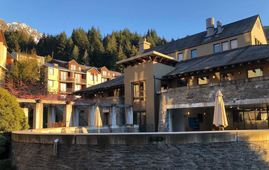 Das Heritage Hotel in Queenstown zeigt eine moderne Architektur, umgeben von üppigem Grün und majestätischen Bergen im Hintergrund.
