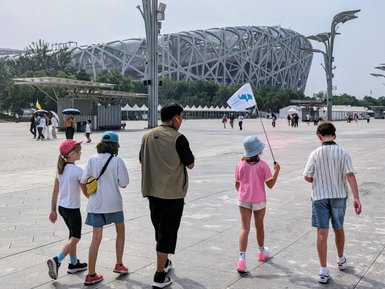 Eine Gruppe von fünf Personen geht über einen weiten Platz vor dem markanten Architekturdesign des Peking Olympiastadions.