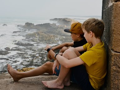 Kinder sitzen nebeneinander und schauen auf das Meer – Marokko mit Kindern