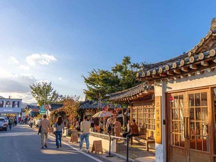 Eine belebte Straße mit traditionellen koreanischen Gebäuden, umgeben von Bäumen und Menschen, die die Atmosphäre genießen.
