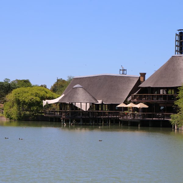 Ein malerisches Lodge-Gebäude mit Strohdach am Ufer eines ruhigen Sees, umgeben von üppigem Grün und klarem Himmel.