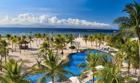 Ein atemberaubender Blick auf einen Pool, umgeben von Palmen und einem weißen Sandstrand unter einem strahlend blauen Himmel.
