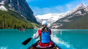 Eine Person paddelt in einem Kanu auf dem türkisfarbenen Wasser des Lake Louise, umgeben von majestätischen Bergen.