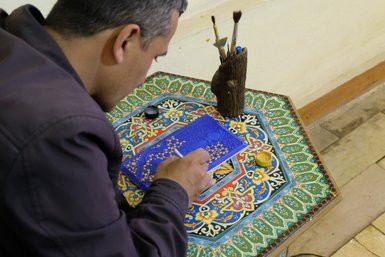 Ein Künstler konzentriert sich auf die Miniaturmalerei, während er feine Details auf einer blauen Fläche hinzufügt.