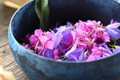Eine Schüssel aus blauem Keramik gefüllt mit bunten, frischen Blumen in verschiedenen Lila- und Rosatönen.