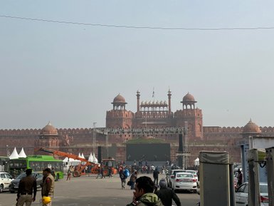 Das Rote Fort in Delhi erhebt sich majestätisch im Hintergrund, umgeben von Menschen und Fahrzeugen auf einer belebten Straße.