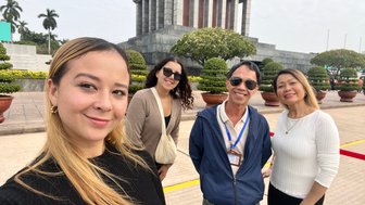 Eine Gruppe von vier Personen posiert fröhlich vor dem Ho-Chi-Minh-Mausoleum, umgeben von gepflegten Pflanzen und einem klaren Himmel.