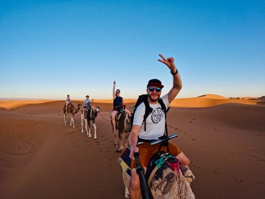 Vater hält einen fröhlichen Moment mit der Familie während einer Kamelkarawane fest – Marokko Reise mit Kindern