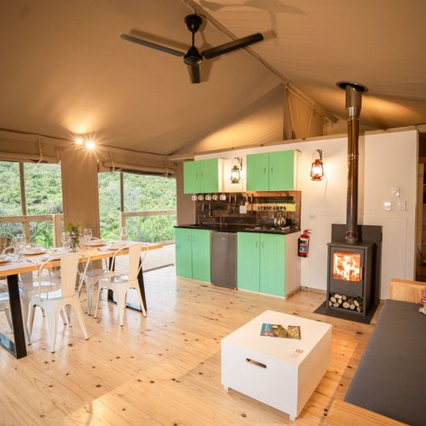 Ein gemütlicher Innenraum mit einem Esstisch, einer modernen Küche und einem Holzofen, umgeben von grüner Natur.