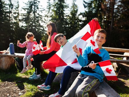 Eine Gruppe von Kindern sitzt im Freien und hält kanadische Flaggen, während sie fröhlich in die Kamera lächeln.
