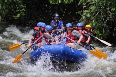 Gruppe paddelt im blauen Rafting-Boot durch Wildwasser – Costa Rica Familienreise