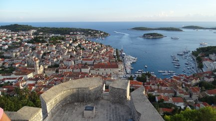 Ein atemberaubender Blick auf die Küstenstadt mit roten Dächern, umgeben von klarem Wasser und kleinen Inseln im Hintergrund.
