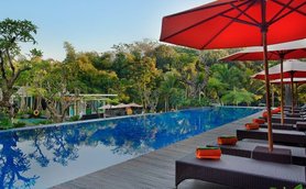 Ein luxuriöser Pool mit reflektierendem Wasser, umgeben von üppigem Grün und Sonnenschirmen in einem tropischen Resort.