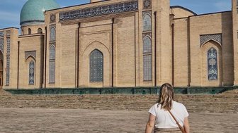 Eine Frau mit langen Haaren geht auf einem Platz vor dem beeindruckenden Hazrati Imam Komplex in Taschkent.