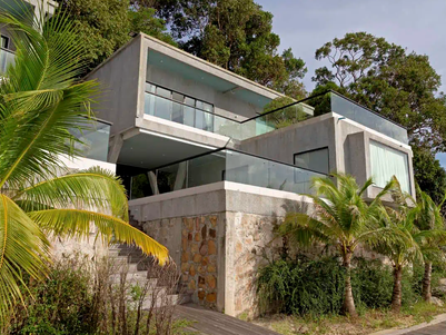 Moderne Villa mit Glasfronten, umgeben von üppigem Grün und Palmen, bietet einen atemberaubenden Blick auf die Natur.