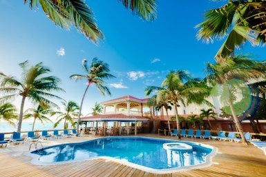 Ein einladender Poolbereich umgeben von Palmen, mit einem klaren blauen Himmel und einem charmanten Hotel im Hintergrund.