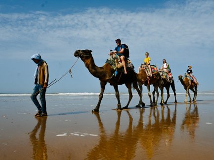 Familie erlebt eine Dromedartour mit Blick auf das Meer entlang der Küste – Marokko mit Kindern