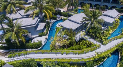 Eine Luftaufnahme eines luxuriösen Resorts mit Palmen, Wasserwegen und modernen Villen in üppiger, grüner Umgebung.