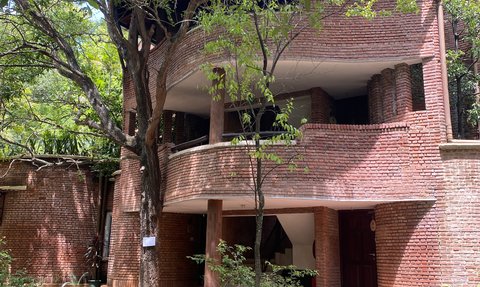 Ein modernes Gebäude mit rotem Ziegelstein, umgeben von üppigem Grün und großen Bäumen, strahlt eine einladende Atmosphäre aus.