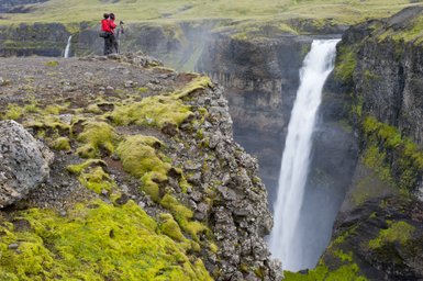 Zwei Fotografen in roten Jacken stehen am Rand einer Klippe und bewundern den majestätischen Haifoss-Wasserfall.