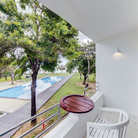 Ein Blick von einem Balkon auf einen ruhigen Pool, umgeben von üppigem Grün und Bäumen, unter einem bewölkten Himmel.