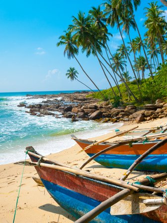 Sandstrand mit Booten neben dem klaren Wasser und Palmen im Hintergrund – Sri Lanka mit Kindern