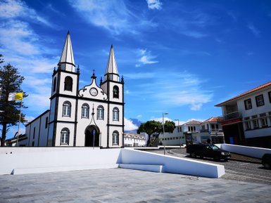Die Igreja de Santa Maria Madalena mit ihren markanten Türmen steht vor einem strahlend blauen Himmel und umgeben von modernen Gebäuden.