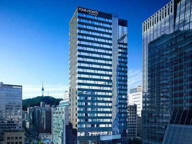 Das moderne Gebäude des Four Points Hotels in Seoul erhebt sich zwischen anderen Wolkenkratzern unter einem klaren blauen Himmel.