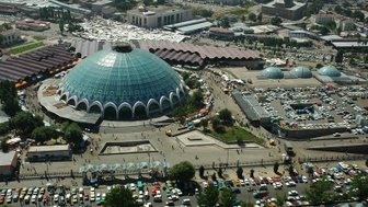 Ein lebhafter Markt mit einem großen, gläsernen Kuppelgebäude im Zentrum, umgeben von Menschen und bunten Ständen.