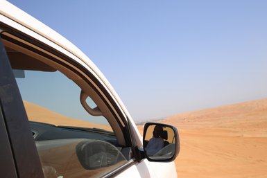 Beduine in der Wahiba-Wüste spiegelt sich im Außenspiegel des Autos – Oman Reise mit Kindern