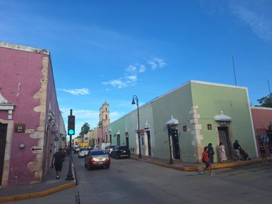 Bunte Gebäude in Valladolid, Mexiko, mit einem grünen und rosa Farbton, unter einem klaren blauen Himmel.