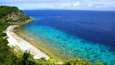 Eine atemberaubende Küstenlandschaft mit klarem, türkisfarbenem Wasser und einem sanften Sandstrand, umgeben von üppigem Grün.