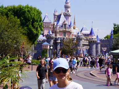 Zwei Kinder stehen vor dem Disneyland-Schloss, umgeben von fröhlichen Besuchern und üppigem Grün.
