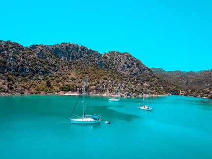 Eine ruhige Bucht in der Türkei mit mehreren Segelbooten, umgeben von grünen Hügeln und klarem, türkisfarbenem Wasser.
