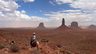 Reiterer auf einem Pferd in Monument Valley, umgeben von beeindruckenden roten Felsen und einem weiten, offenen Himmel.