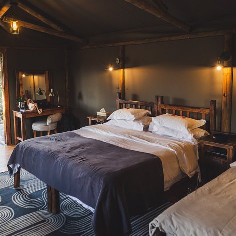 Ein gemütliches Zimmer mit zwei Betten, rustikalen Holzmöbeln und einem modernen Teppich, der dem Raum Charakter verleiht.
