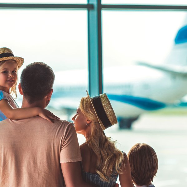 Eine Familie steht am Flughafen und beobachtet ein Flugzeug, während das kleine Mädchen auf dem Arm des Vaters sitzt.
