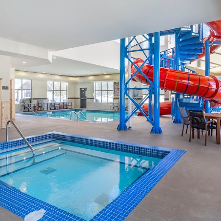 Ein helles Hallenbad mit einem großen Wasserrutschen und einem Whirlpool, umgeben von modernen Möbeln und Fenstern.