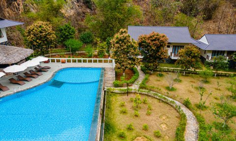 Ein atemberaubender Blick auf einen blauen Pool, umgeben von üppigem Grün und modernen Bungalows in einer ruhigen Berglandschaft.