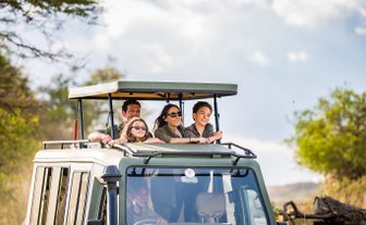 Familie erkundet mit Guide die Tierwelt in einem Safarijeep – Tansania mit Kindern
