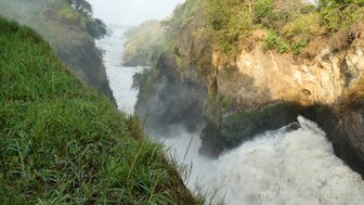 Ein beeindruckender Wasserfall stürzt in eine enge Schlucht, umgeben von üppigem Grün und nebligen Sprühnebel.