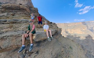 Familie macht eine Pause auf einem Felsen und blickt über die beeindruckende Schlucht des Jebel Shams – Oman mit Kindern