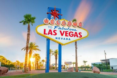 Das berühmte Willkommensschild von Las Vegas strahlt in leuchtenden Farben, umgeben von Palmen und einem klaren Himmel.