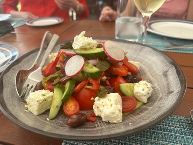 Ein bunter Salat mit Tomaten, Gurken, Paprika und Feta-Käse, serviert auf einem grauen Teller mit Besteck.