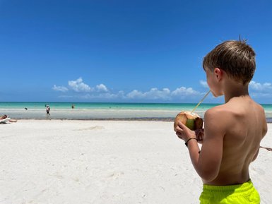 Kind trinkt frisches Kokosnusswasser am Strand von Puerto Morelos – Mexiko Familienreise