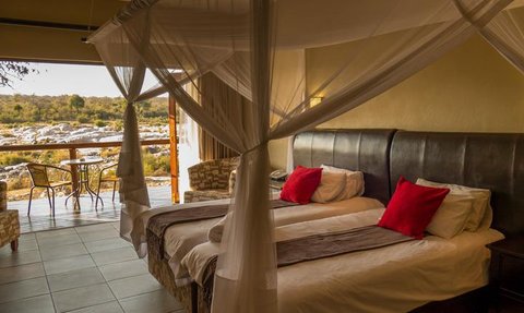 Ein elegantes Zimmer mit zwei Einzelbetten, dekoriert mit roten Kissen und einem Blick auf die Natur durch große Fenster.