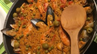Ein köstlicher Teller Paella mit Garnelen, Muscheln und Erbsen, serviert in einer großen Pfanne auf einem grünen Tisch.