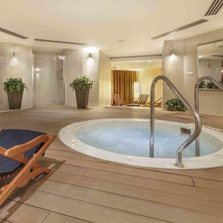 Ein eleganter Wellnessbereich mit einem Mini-Pool, umgeben von Pflanzen und einem bequemen Liegestuhl aus Holz.