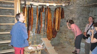 Eine Person betrachtet mit Interesse die an der Wand hängenden, getrockneten Fleischstücke in einem steinernen Raum.